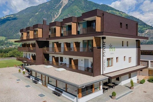 Moderný hotel s drevenými balkónmi na pozadí horského masívu.  