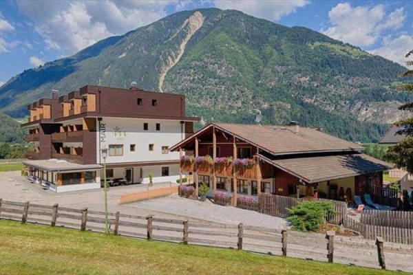 Horský hotel s drevenými balkónmi plnými kvetov na úpätí zelenej hory.  