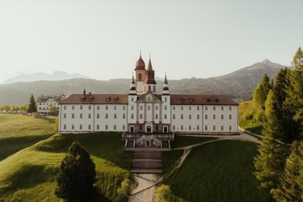 Kláštor na vrchole zeleného kopca s horami v pozadí.