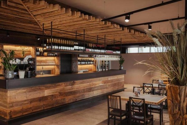 Moderný bar s drevenými prvkami a vystavenými fľašami vína.