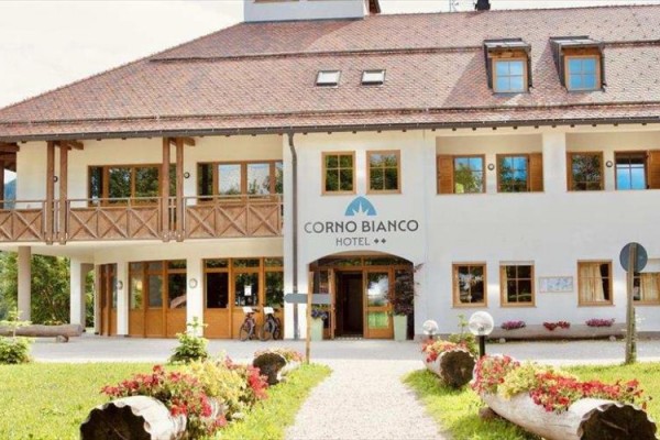 Hotel Corno Bianco s drevenými prvkami a kvetmi pred vstupom.