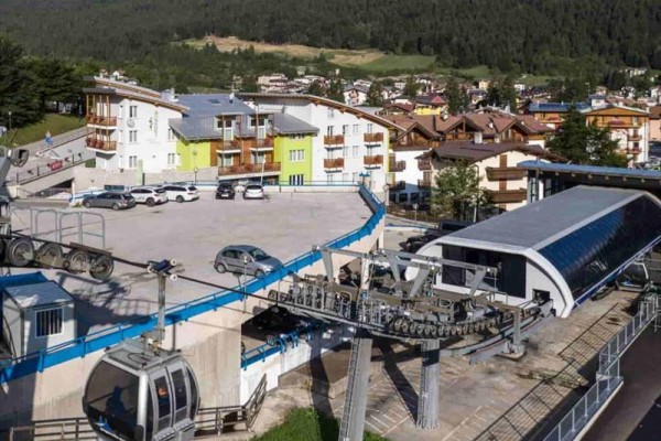 Lanovka pri horskom mestečku s autami na parkovisku a kopcami v pozadí.  
