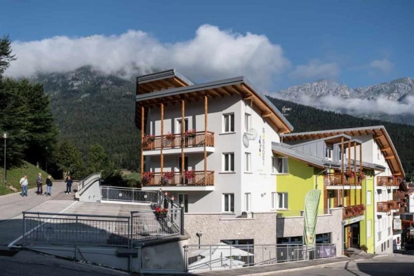 Moderný hotel v horskej krajine s modrou oblohou a oblakmi.