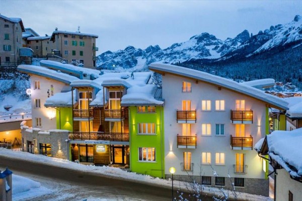 Moderný hotel so zasneženou strechou na pozadí horského panorámy.