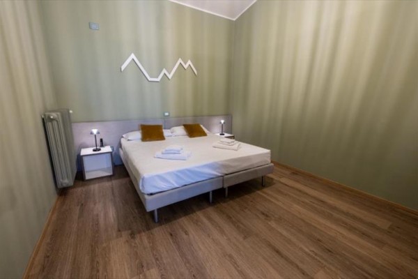 Moderná spálňa s manželskou posteľou, dvoma lampičkami a dekoráciou na stene.