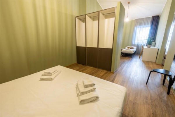 Moderná spálňa s posteľou, skriňou a poskladanými uterákmi na drevenej podlahe.