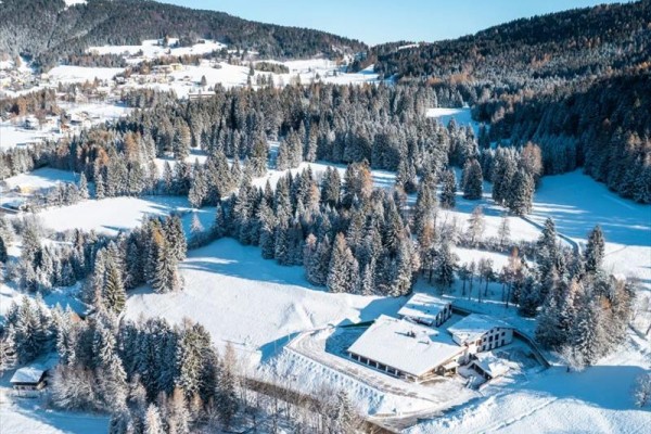 Zasnežená krajina s lesmi a kopcami pod modrou oblohou.