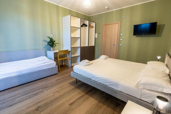 Moderná hotelová izba s manželskou posteľou, jednolôžkom, skriňou a televízorom na stene.