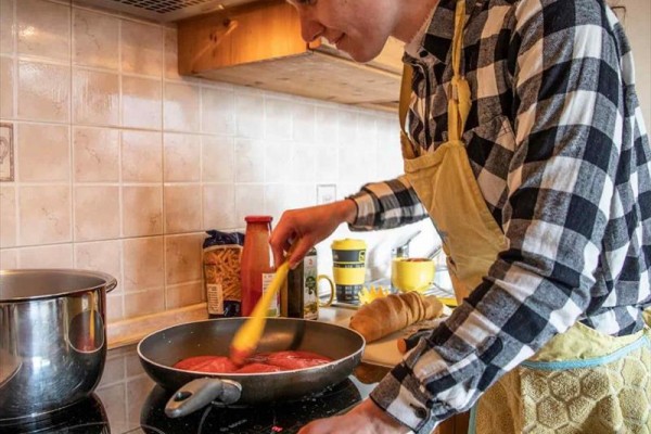 Osoba miešajúca paradajkovú omáčku na panvici v kuchyni.