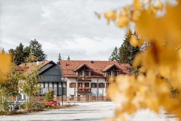 Budova s červenou strechou obklopená jesennými stromami.