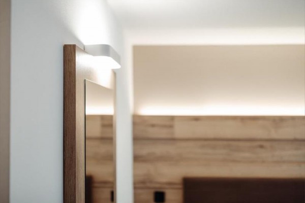 Drevený rám zrkadla a moderná nástenná lampa v interiéri izby.