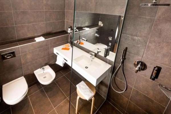 Moderná kúpeľňa s tmavými dlaždicami, sprchovým kútom, umývadlom a toaletou.