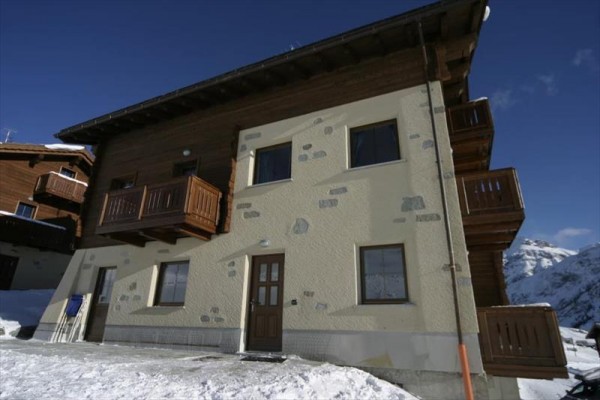 Dvojposchodová horská chata s drevenými balkónmi na zasneženej krajine.  