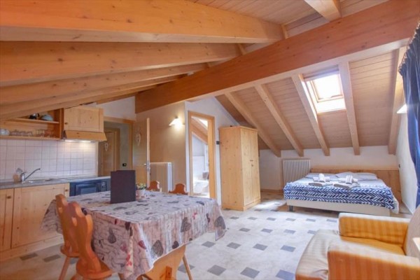 Podkrovný apartmán s dreveným stropom, kuchynským kútom, jedálenským stolom a posteľou.
