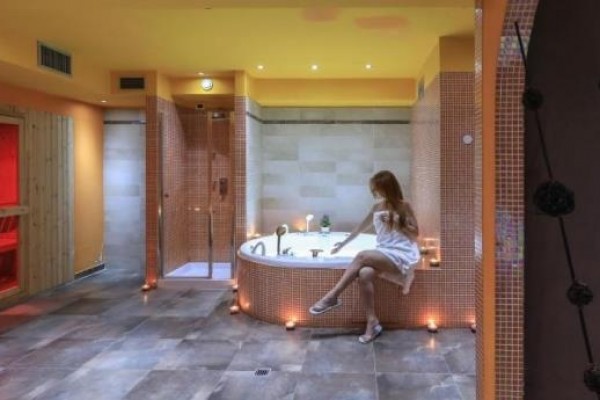 Wellness miestnosť s vírivkou a infrasaunou, kde sedí žena v bielom uteráku.