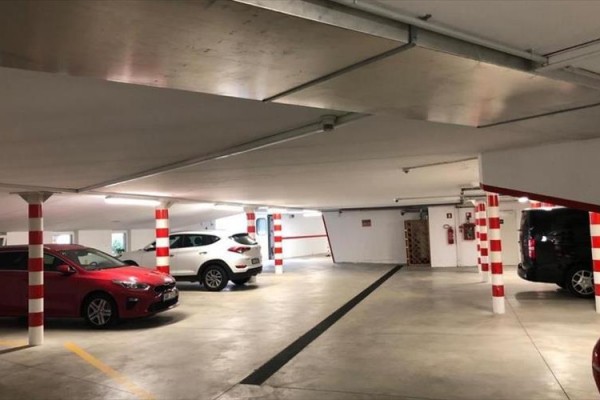 Podzemná garáž s autami a stĺpmi s červeno-bielymi pruhmi.