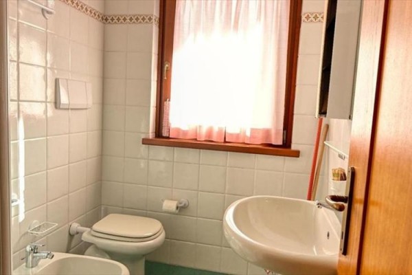 Kúpeľňa s umývadlom, toaletou a oknom s bielymi závesmi.