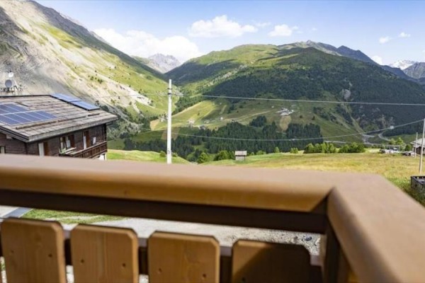 Horská panoráma s domom so solárnymi panelmi a zelenými kopcami v pozadí.