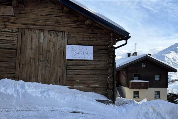 Drevená chata na zasneženej stráni vedľa ďalšej horskej chaty.