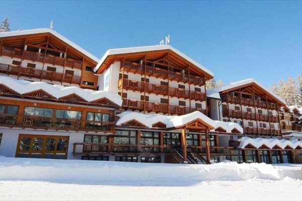 Veľký horský hotel s drevenými balkónmi pokrytý snehom za slnečného dňa.
