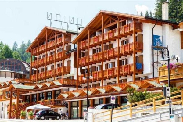 Horský hotel s drevenými balkónmi a strešnou konštrukciou, obklopený stromami.